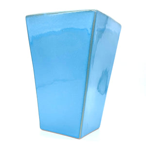 Das Bild zeigt ein eckiges Gefäß in der Farbe blau. Dieses Behältnis kann man mit Blumen befüllen.
