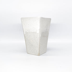 Auf dem Bild ist eine weiße Blumenvase zu sehen. Das Gefäß wurde aus Keramik hergestellt.