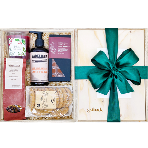 Unsere Winterzauber Box (M) ist mit Winterpunsch Tee, Weihnachtskerze, Vanille Kipferl, Sweet Orange Handseife, und köstlicher Schokolade gefüllt. Links siehst du die Box mit den Produkten offen da liegen. Rechts davon siehst du die Box geschlossen mit grüner Schleife und den Namen givtback eingraviert. 