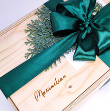 Lade das Bild in den Galerie-Viewer, All unsere Holzboxen können mit deinem Wunschnamen graviert werden. Die Namen werden auf der Vorderseite des Deckels eingraviert. Dadurch wird dein Geschenk persönlicher und besonderer. Die Schriftart kannst du nach deinen persönlichen Wünschen aussuchen. Hier siehst du einige Beispiele wie der eingravierte Name aussehen könnte.  Hier siehts du eine Holzkiste mit dem Namen &quot;Maximilian&quot; eingraviert. Die Holzkiste ist mit einer grünen Schleife gebunden mit einem Tannenzweig darunter. 
