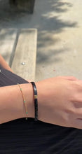 Laden und Abspielen von Videos im Galerie-Viewer, Im Video ist eine Hand mit Armbändern zu sehen. Die Frau trägt zwei verschiedene Armbänder. Das erste Armband ist schwarz und dick. Sie besteht nur aus schwarzen, rechteckigen, flachen Steinchen. In der Mitte stechen zwei goldene Steinchen auf. Das zweite Armband besteht aus einer goldenen Armkette mit türkisen Steinchen.
