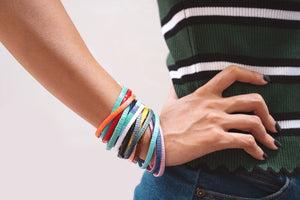 Hier siehst du eine Hand mit vielen verschiedenen farbigen Armbändern