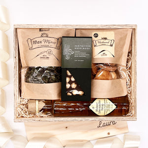  Unsere Geschenkboxen sind immer ein gutes Geschenk für jeden Anlass. Unsere Feinschmecker Box ist hier abgebildet mit Bio Tee, Heidesand Kekse, Schokolade und Löwenzahnsirup in einer offenen Holzbox.